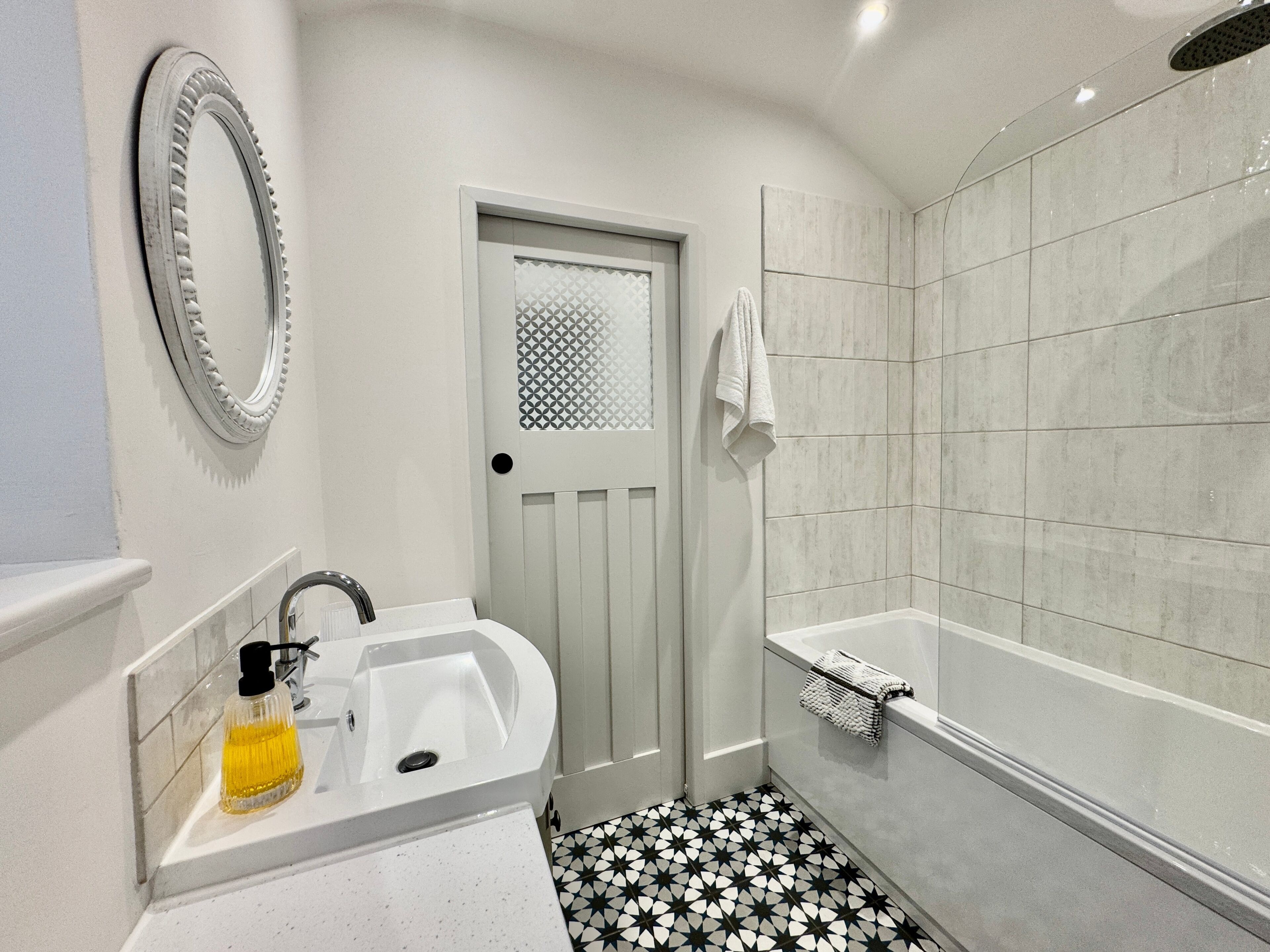Un bagno con lavandino bianco, uno specchio, una doccia e una porta con motivo geometrico.