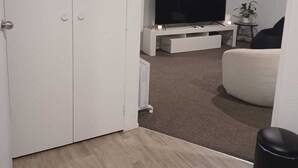 A modern living room with a white door, a flat-screen TV, a white sofa, and a small table with a plant.
