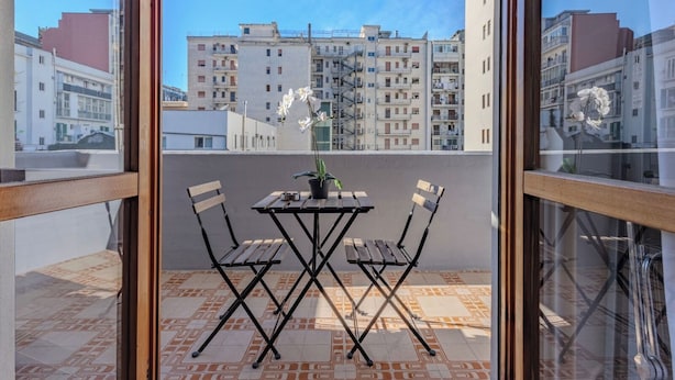 A balcony with a table and chairs, a potted plant, and a view of apartment buildings. - Andrea's home Bari (Bari)