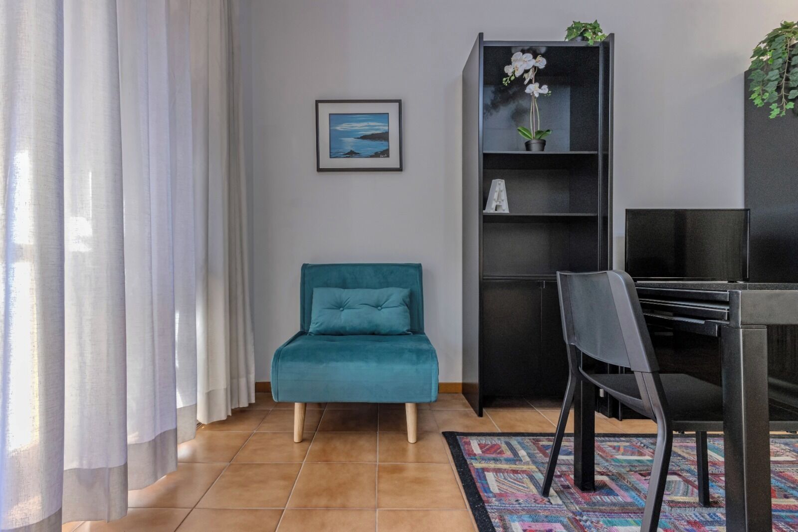 A modern living room with a teal sofa, a black entertainment unit, and a framed picture on the wall.