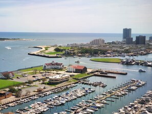 A marina with numerous boats docked, a large building with a red roof, and a cityscape in the background.