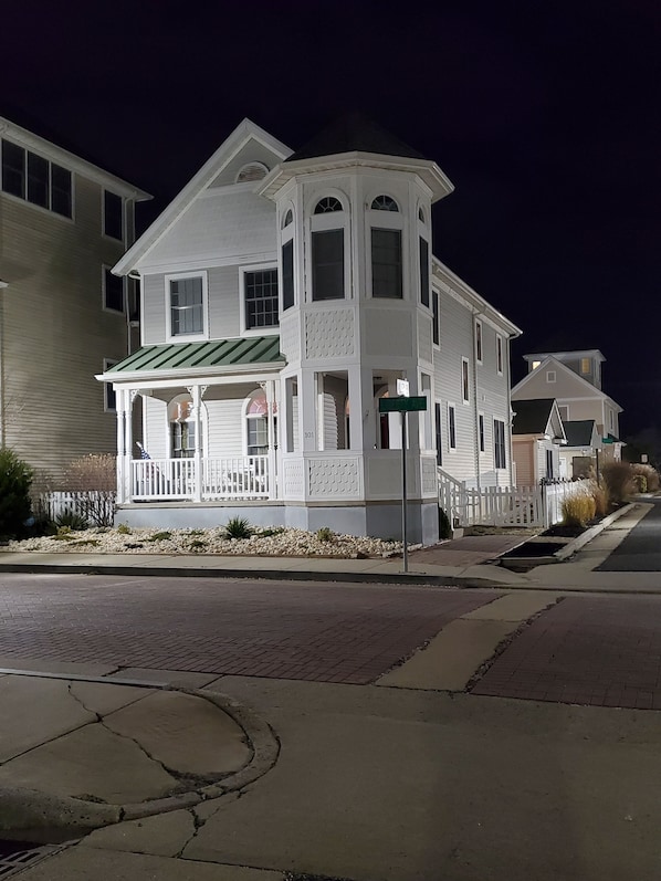A two-story house with a porch and a green awning, located on a residential street at night.