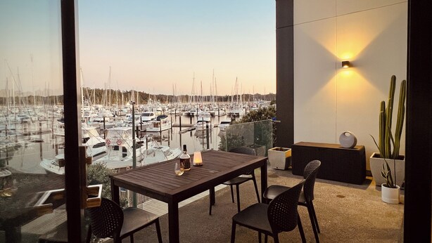 Un balcon avec une table et des chaises, donnant sur une marina où sont amarrés des bateaux.