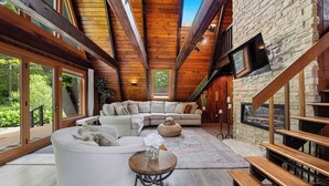 A spacious living area with a large sectional sofa, a round wooden coffee table, and a stone wall. - Rustic A Frame Cabin. Nature retreat on 4 acres! 15 minutes from 3 waterfalls (LaFayette)