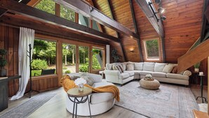 A spacious loft bedroom with a large window, a curved sofa, a round table, and a wooden ceiling. - Rustic A Frame Cabin. Nature retreat on 4 acres! 15 minutes from 3 waterfalls (LaFayette)