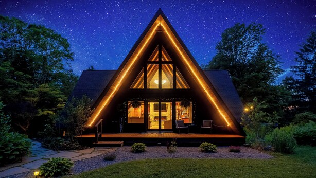 A triangular-shaped house with large windows and a well-lit interior, surrounded by a garden and trees. - Rustic A Frame Cabin. Nature retreat on 4 acres! 15 minutes from 3 waterfalls (LaFayette)