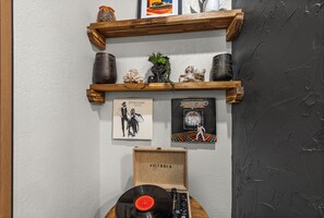 Un mur orné d’étagères en bois où sont disposés des objets décoratifs, des œuvres d’art encadrées et une platine vinyle.