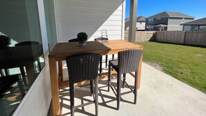 Une terrasse avec une table en bois et deux chaises en osier, une petite plante en pot et un porte-chaises en métal.