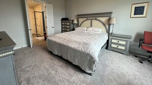 Une chambre à coucher comprenant un lit, une commode, une table de chevet, une chaise et un ventilateur de plafond.