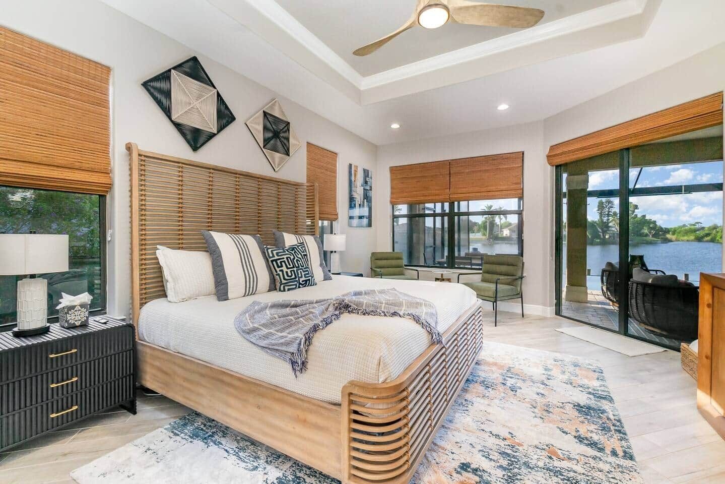 A spacious bedroom with a large bed, a wooden headboard, a nightstand, and a view of a lake through large windows.