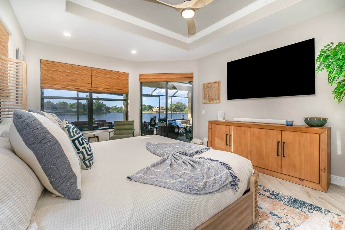 A bedroom with a large bed, a TV mounted on the wall, and a view of a lake through the window.