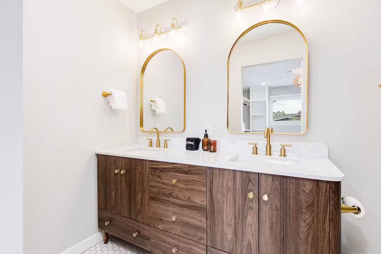 Ein modernes Badezimmer mit zwei Waschbecken, goldenen Armaturen und Holzunterschränken.