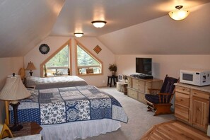 A cozy attic bedroom with a large bed, a TV, and a microwave.