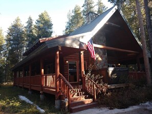 A log cabin with a porch, a stone chimney, and an American flag.