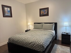 A neatly arranged bedroom with a bed, two bedside tables, a nightstand, a lamp, and two framed pictures on the wall.