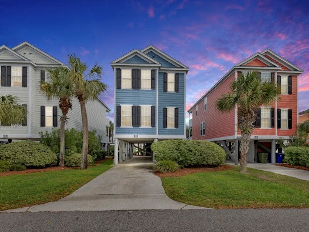 A row of three-story townhouses with a central walkway, each with a front porch and palm trees.