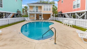 A swimming pool surrounded by white fences, with two buildings in pastel colors on either side.