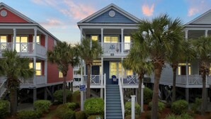 A row of waterfront condominiums with balconies, a central staircase, and palm trees.