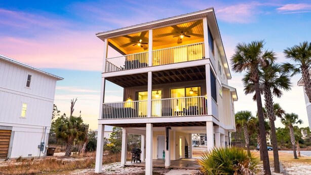 Ein zweistöckiges Strandhaus mit Balkonen, einer Veranda und sandigem Untergrund.