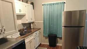 A kitchen with white cabinets, a stainless steel refrigerator, a sink, and a trash can. - 3-bedroom house in charming Magnolia with AC (Magnolia)