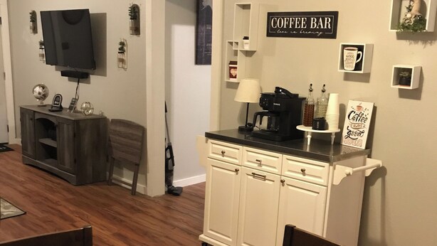 A dining area with a wooden table, chairs, a coffee station, and a television in the background. - 3-bedroom house in charming Magnolia with AC (Magnolia)