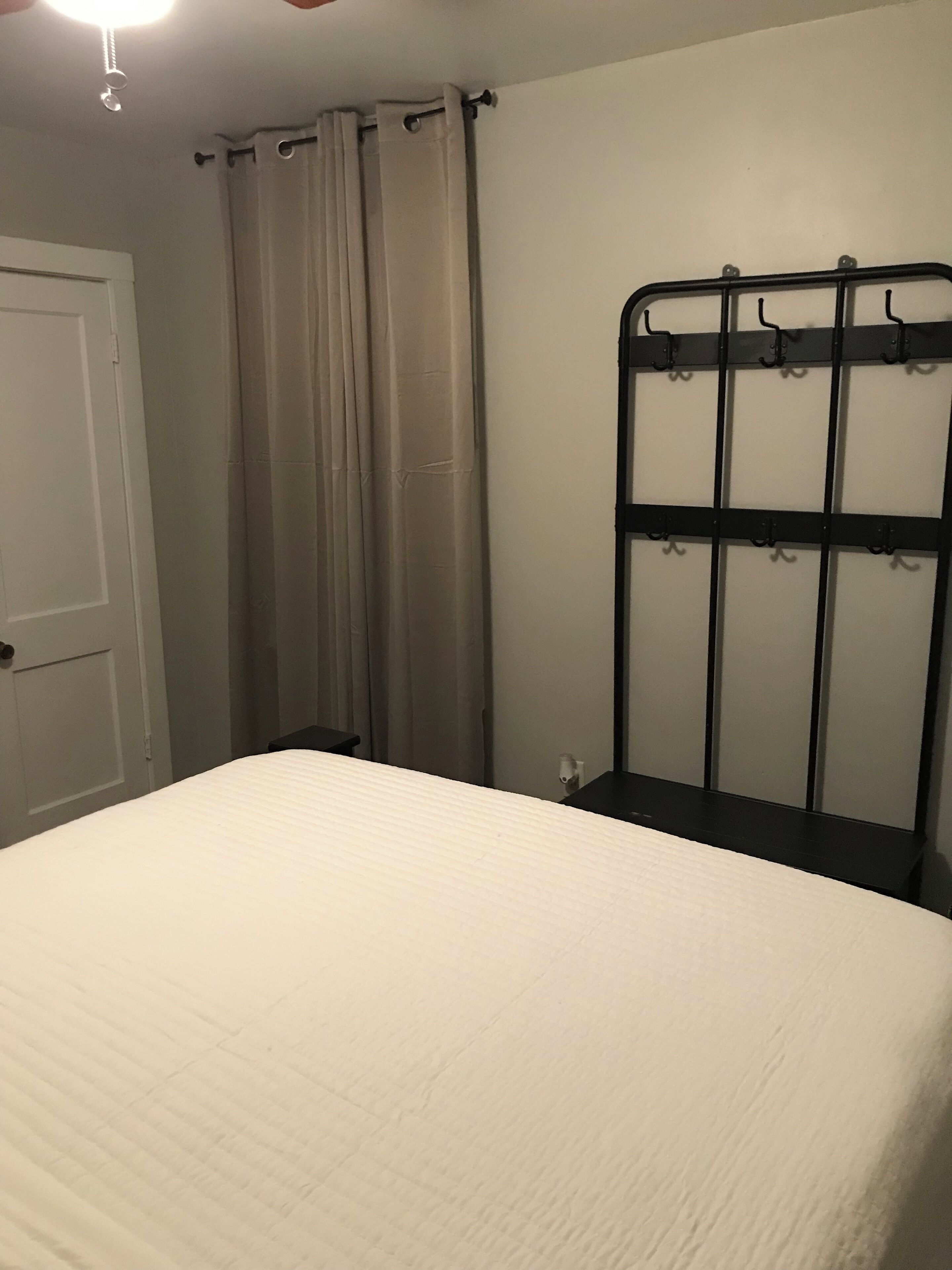 Une chambre à coucher avec un lit, une porte, un rideau et un cadre de lit en métal muni de crochets.