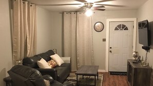 A living room with a leather sofa, a coffee table, a ceiling fan, a door, and a television on a stand. - 3-bedroom house in charming Magnolia with AC (Magnolia)