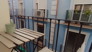Un balcone con una sedia e un tavolo, una finestra che si affaccia sulla facciata dell'edificio e una ringhiera in metallo.