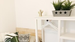 Un letto rifatto con cuscini decorati, un comodino bianco con un cactus e decorazioni a forma di stella, e una mensola sospesa.