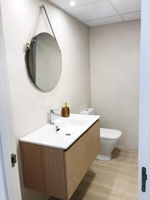 A modern bathroom with a white sink, wooden vanity, and a toilet. - Suite Estébanes (Zaragoza)