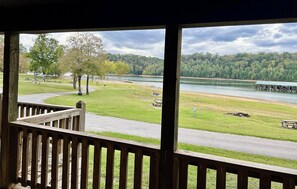 A view from a wooden deck overlooking a grassy area with a lake, picnic tables, and a covered boat launch area. - 3 Bedroom charming Cabin on Dale Hollow Lake at Wolf River Resort and Marina (Albany)