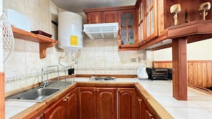 A kitchen with wooden cabinets, a built-in sink, a stove, and a water heater. - Volcano shelter. 1 km from downtown! (Araucanía)