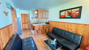 A living room with a black leather sofa, a glass coffee table, and wooden paneling. - Volcano shelter. 1 km from downtown! (Araucanía)
