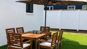 Un patio con una mesa y sillas de madera, una sombrilla y una cerca blanca al fondo.