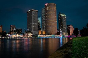 Lo skyline di una città con moderni grattacieli, una passeggiata sul lungomare e un ponte illuminato da luci colorate.