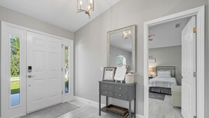 A hallway with a grey console table, a mirror, and a door leading to a bedroom. - Newly Remodeled, Spacious 4-Bedroom Getaway (Palm Coast)