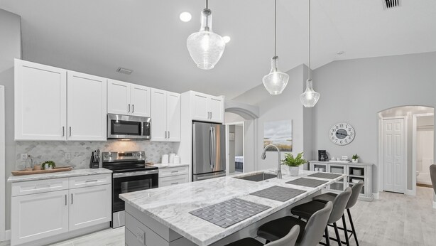 A modern kitchen with white cabinets, a central island with bar stools, stainless steel appliances, and pendant lighting. - Newly Remodeled, Spacious 4-Bedroom Getaway (Palm Coast)