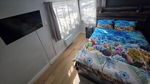 Ett sovrum med en säng, en tv som är monterad på väggen, en värmare och ett fönster med gardiner.