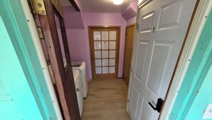 A narrow hallway with wooden flooring, a door with frosted glass panels, and a white door with a black handle.