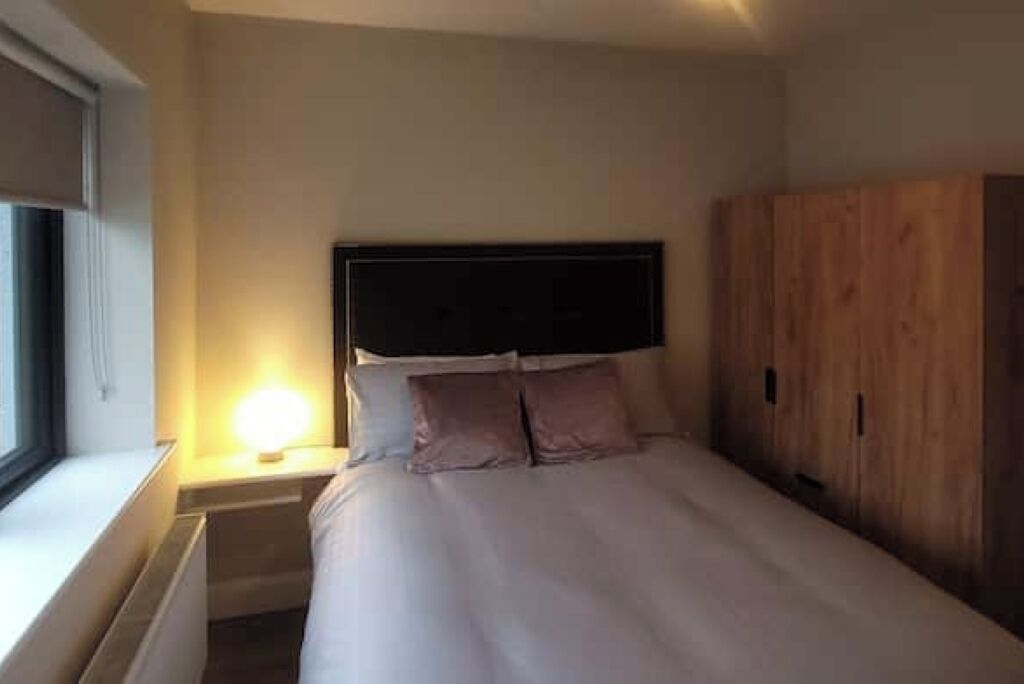 Una camera da letto con un letto, un comodino con una lampada, un armadio in legno e una finestra.