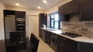 Une cuisine moderne avec des meubles de rangement de couleur sombre, un four encastré, une cuisinière à gaz et un lave-linge.