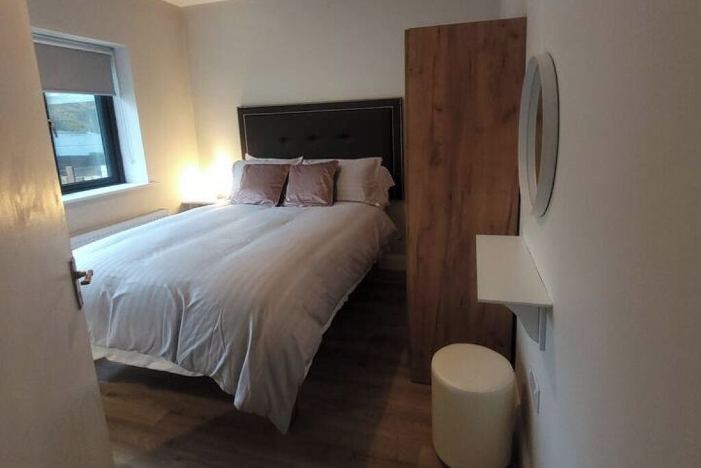 Une chambre avec un lit, un mur recouvert de panneaux en bois, un petit tabouret rond et une fenêtre.