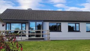 Une maison moderne à deux étages, avec un toit en tuiles, de grandes fenêtres et une pelouse verdoyante.