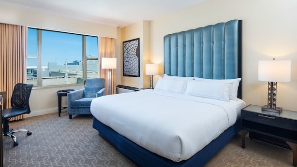 A hotel room with a large bed, a desk, a chair, and a view of the cityscape. - The Marc Hotel (Milwaukee)