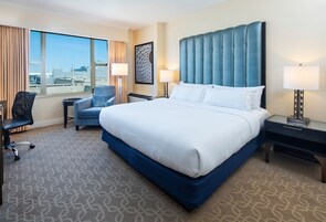 Habitación de hotel con una cama grande, un escritorio, una silla y vistas a la ciudad.