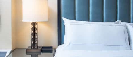 Un lit bien fait, avec du linge de lit blanc et une tête de lit bleue, une table de chevet avec une lampe et un petit tiroir.