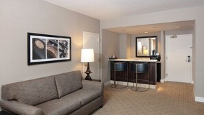 A hotel room with a sofa, a framed picture, a lamp, a minibar, and a mirror. - The Marc Hotel (Milwaukee)