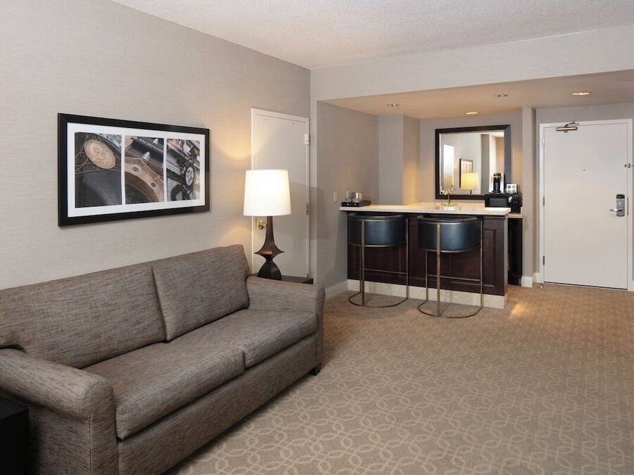 Ein Hotelzimmer mit einer Couch, einem gerahmten Bild, einer Lampe, einer Minibar und einem Spiegel.