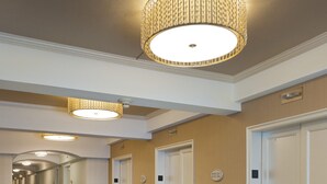 A hotel hallway with a patterned carpet, multiple doors, and a decorative ceiling light fixture. - The Marc Hotel (Milwaukee)