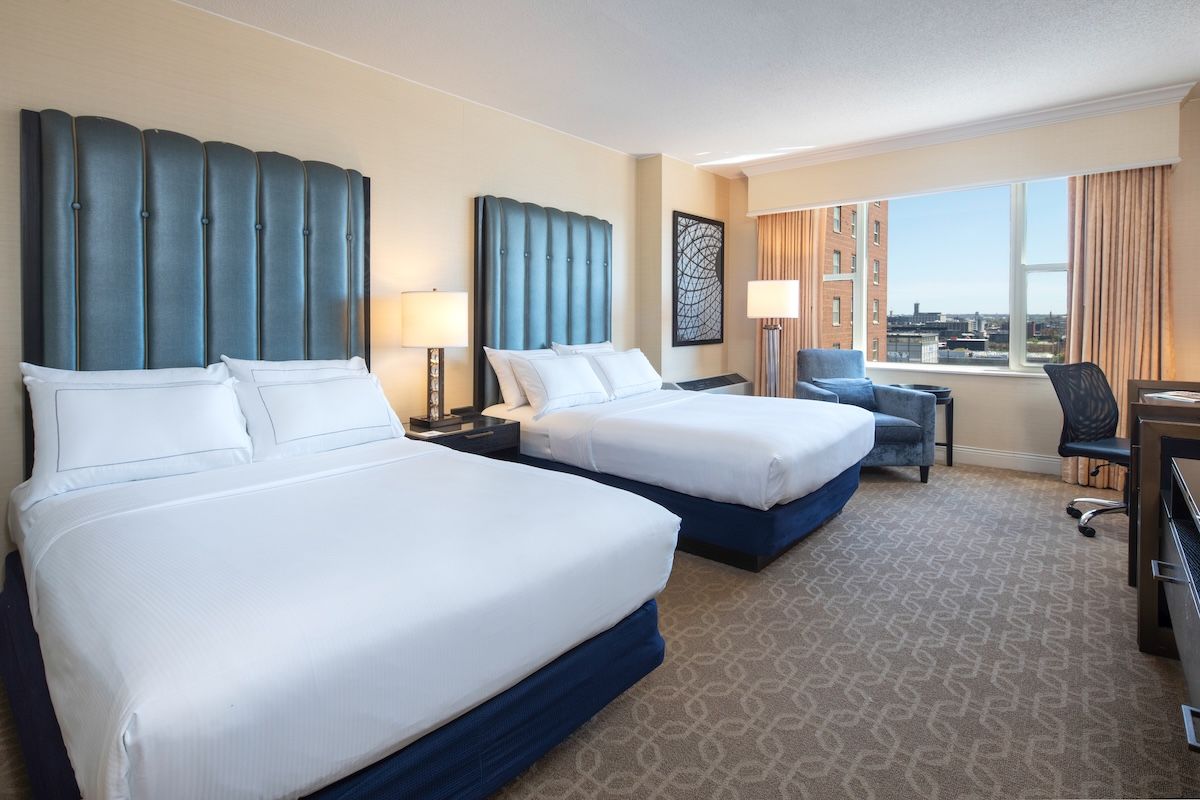 A hotel room with two beds, a desk, and a view of the city.